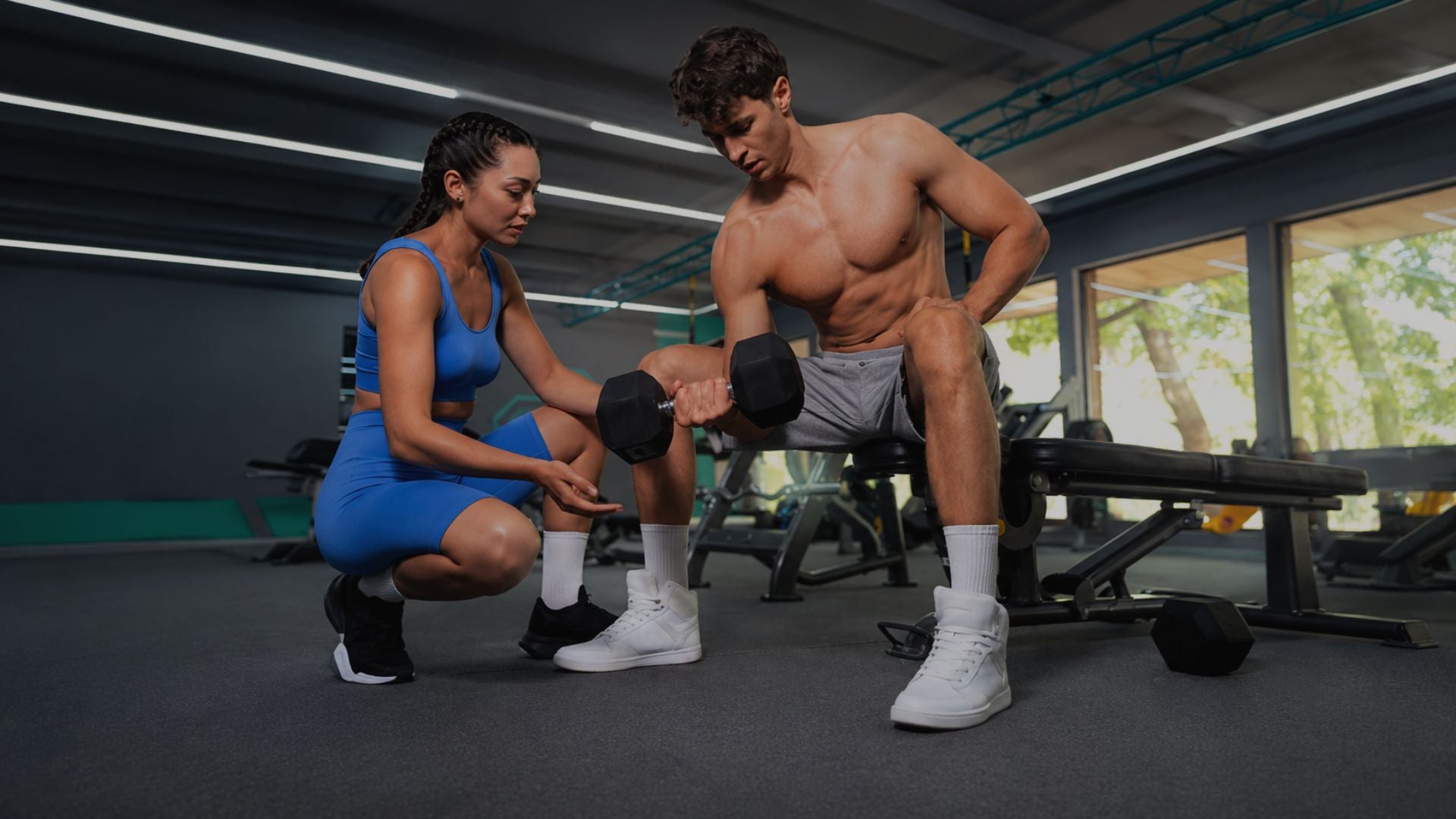 Two people in a gym setting, one assisting the other with exercise equipment.